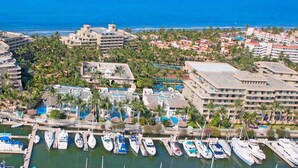 An aerial view of a coastal marina with multiple boats docked, surrounded by hotels and lush greenery. - PARADISE VILLAGE RESORT 2 BEDROOM ONE WEEK MAX (Nuevo Vallarta)