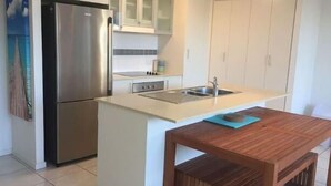 A compact kitchen with a stainless steel refrigerator, a sink, and a wooden table. - Perch Apartments at Anembo Street (Surfers Paradise)