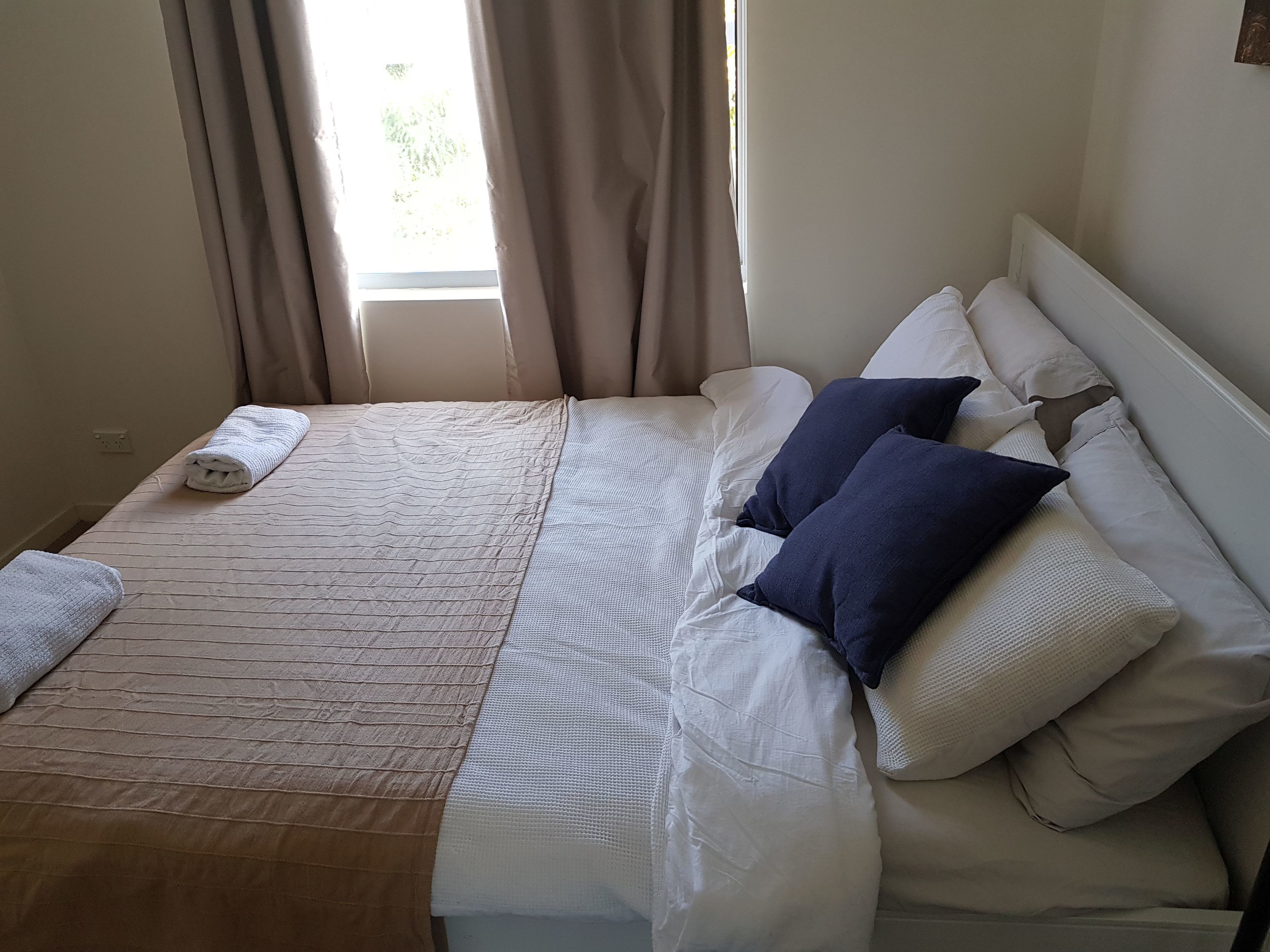 A neatly made bed with a patterned bedspread, two pillows, and a folded towel.