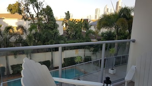 A balcony with a pool, white chairs, and a lantern. - Perch Apartments at Anembo Street (Surfers Paradise)