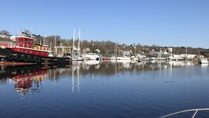 En havn med en rød slæbebåd ved kaj, omgivet af roligt vand der spejler både og bygninger.