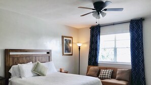 A bedroom with a bed, a headboard, a bedside table, a lamp, a window with curtains, and a ceiling fan. - Studio Suite - Minutes from everything (Dania Beach)