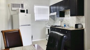 A compact kitchen with a refrigerator, stove, microwave, and black cabinets. - Studio Suite - Minutes from everything (Dania Beach)