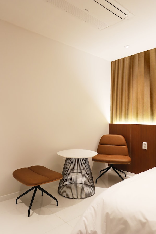 A modern hotel room with a bed, a round table, two chairs, and a wall-mounted light fixture. - Biennale Hotel (Gwangju)