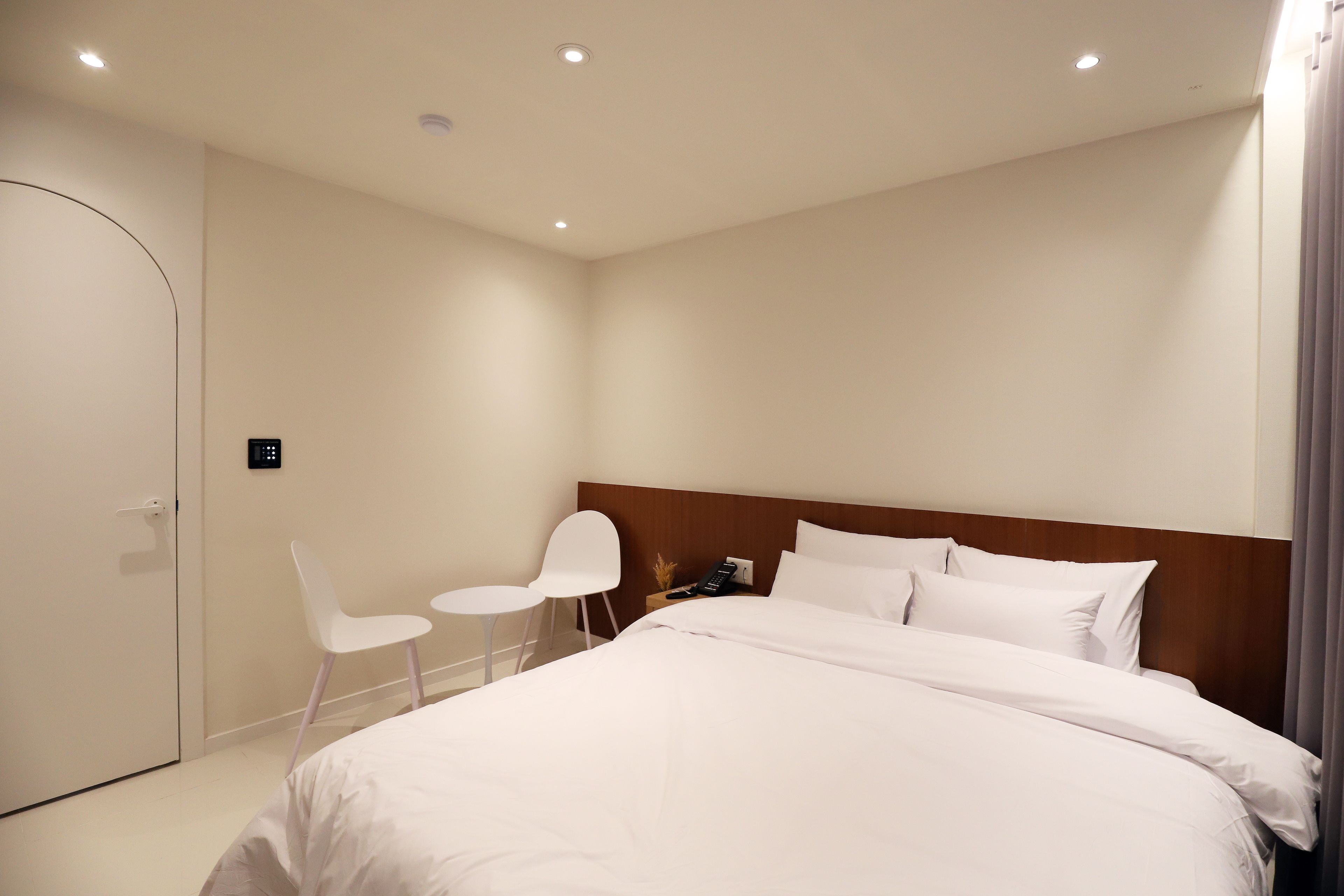 A hotel room with a large bed, a wooden headboard, a small desk with a chair, and a door.