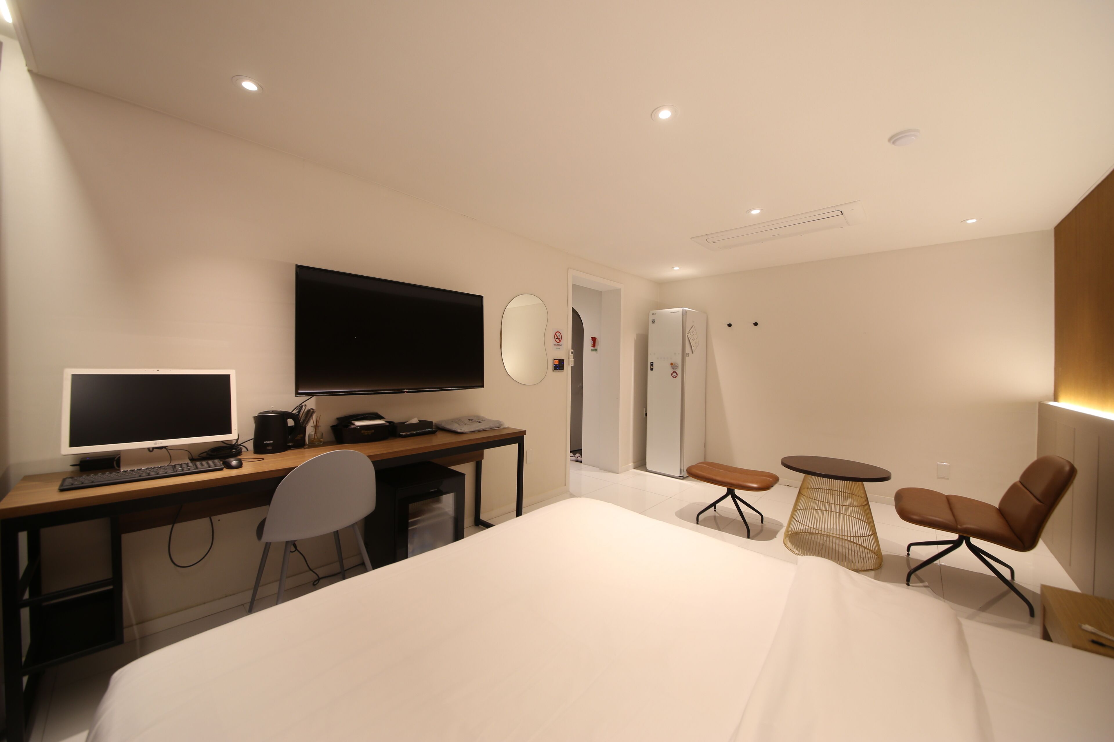 Quarto de hotel moderno com uma cama grande, uma escrivaninha com computador, televisão de tela plana, espelho, mesa pequena e uma cadeira.