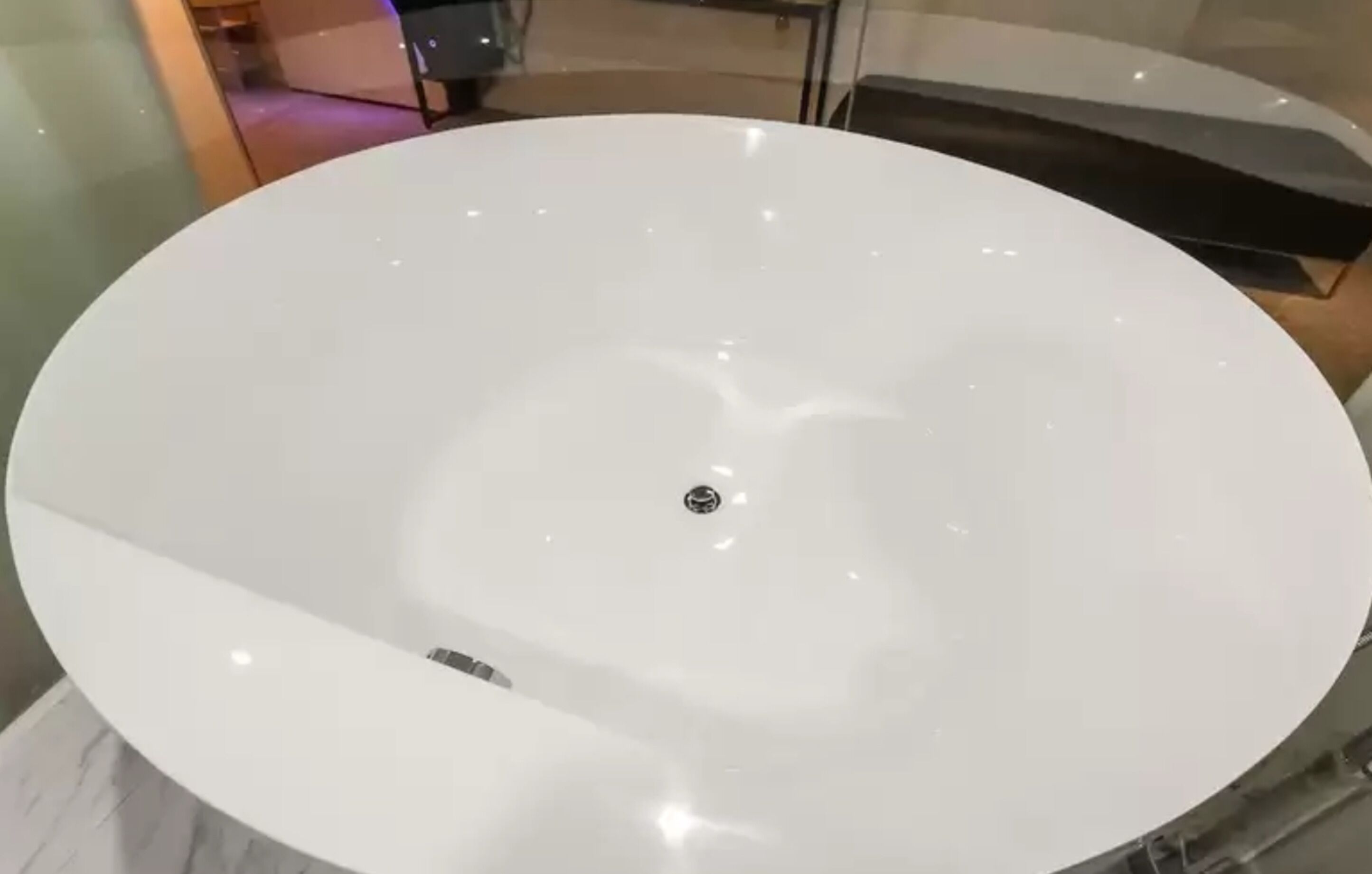 A large, round, white bathtub with a central drain.