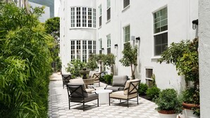 Un patio con mobiliario exterior, plantas en macetas y un edificio blanco con ventanas amplias.