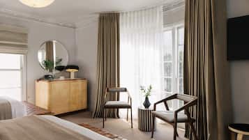 Une chambre d’hôtel avec un grand lit, deux chaises, une armoire en bois, un miroir rond et un téléviseur fixé au mur.
