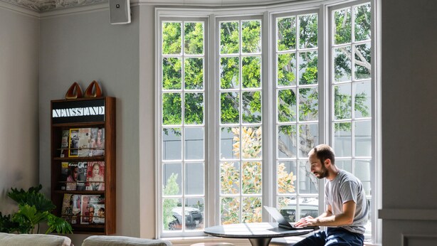 Una habitación con un amplio ventanal, una estantería de madera y una mesa redonda con un ordenador portátil.