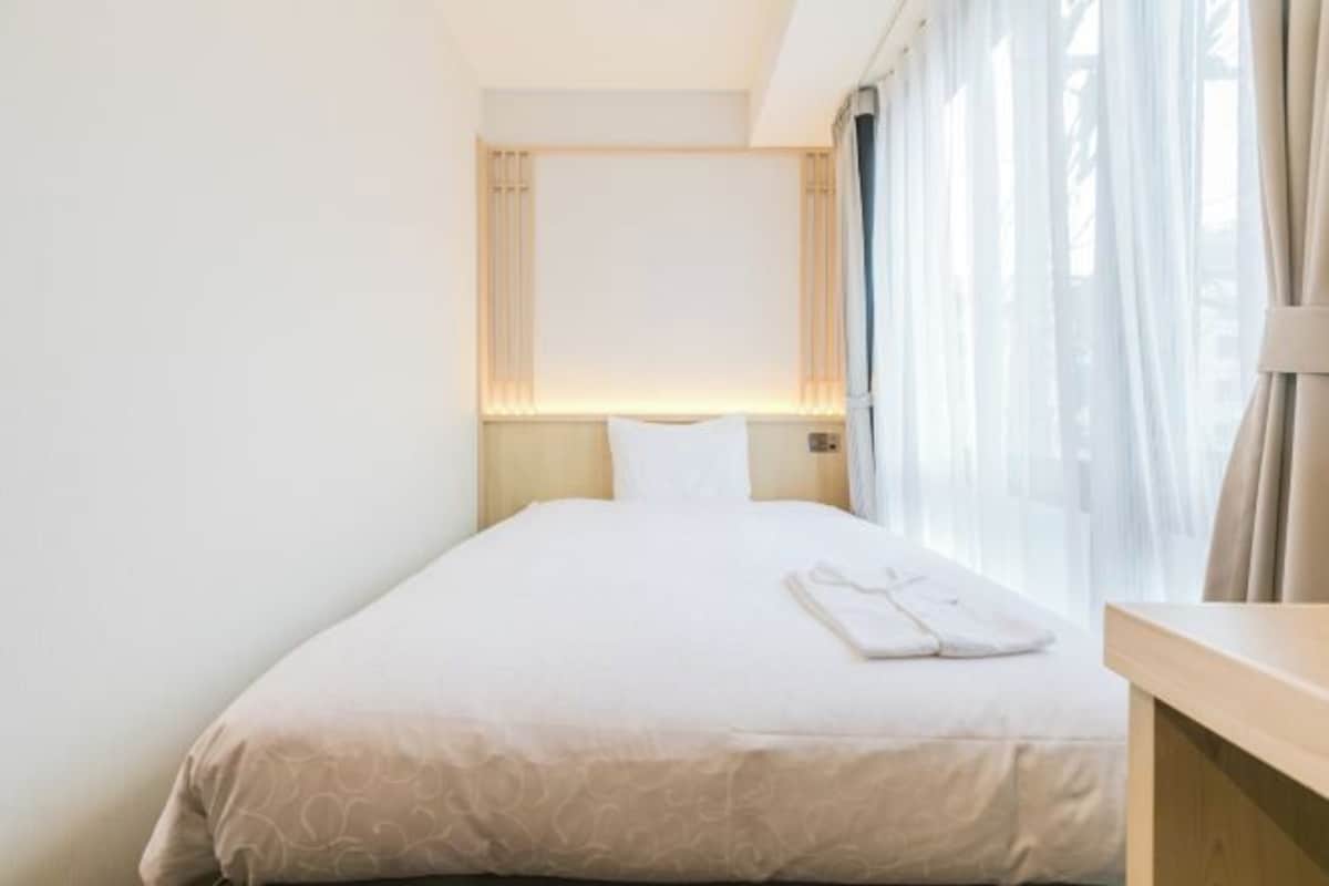 A hotel room with a neatly made bed, a bedside table, and a window with curtains.