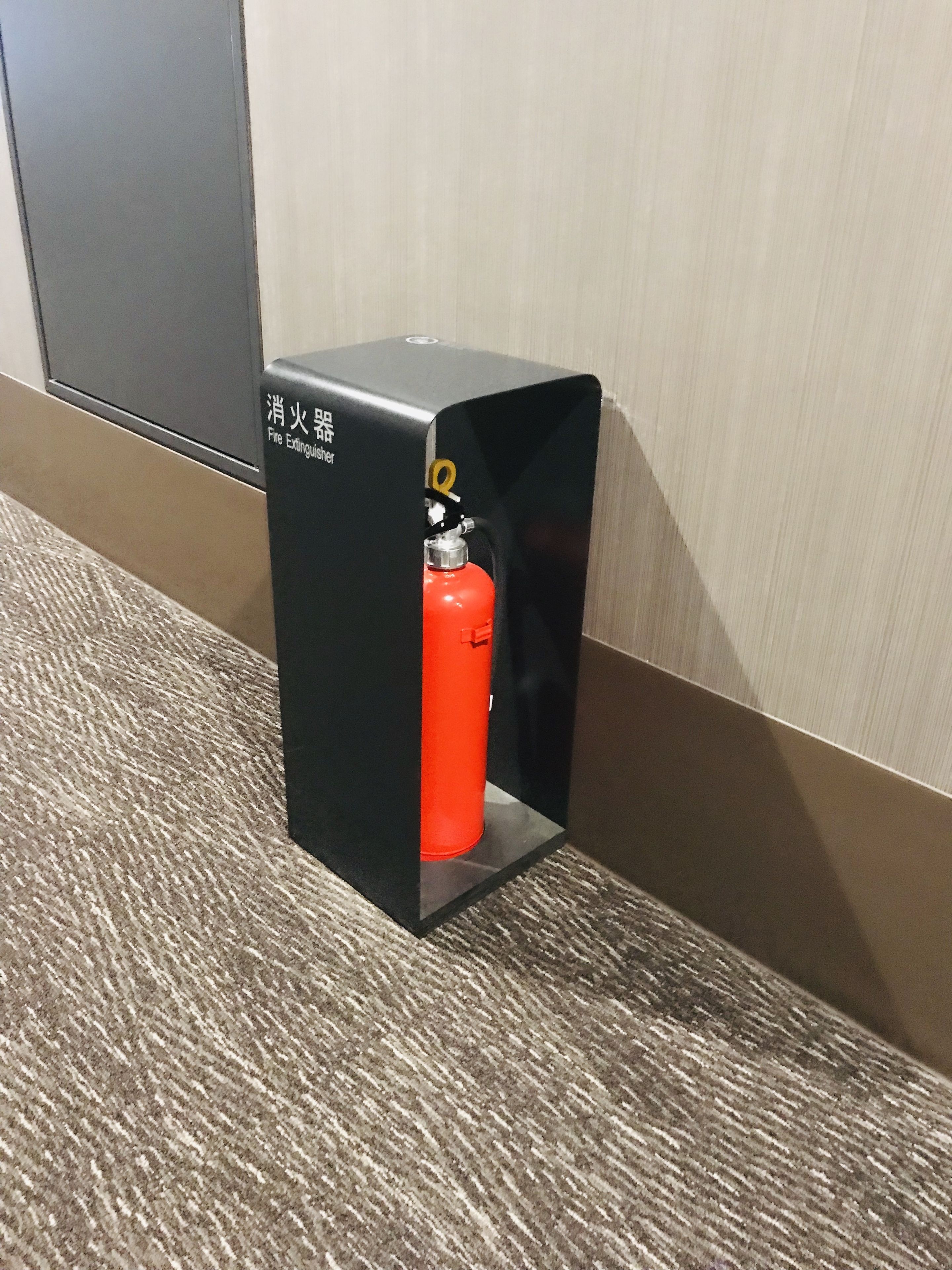 A fire extinguisher mounted on a black stand in a hallway.