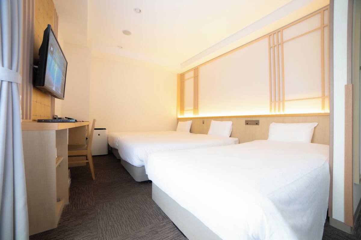 Et hotelværelse med to senge, et skrivebord, et fjernsyn og et klædeskab.