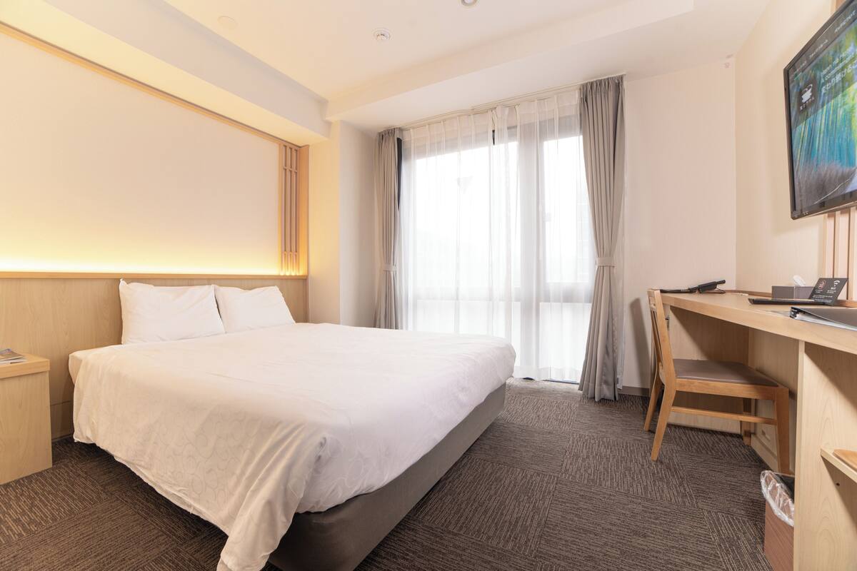 Et hotelværelse med seng, skrivebord, stol og fjernsyn på væggen.