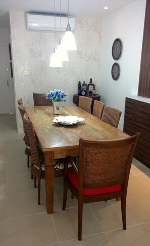 Cozy dining area with a long table and six chairs, featuring a pendant light fixture and bamboo leaf pattern wallpaper.