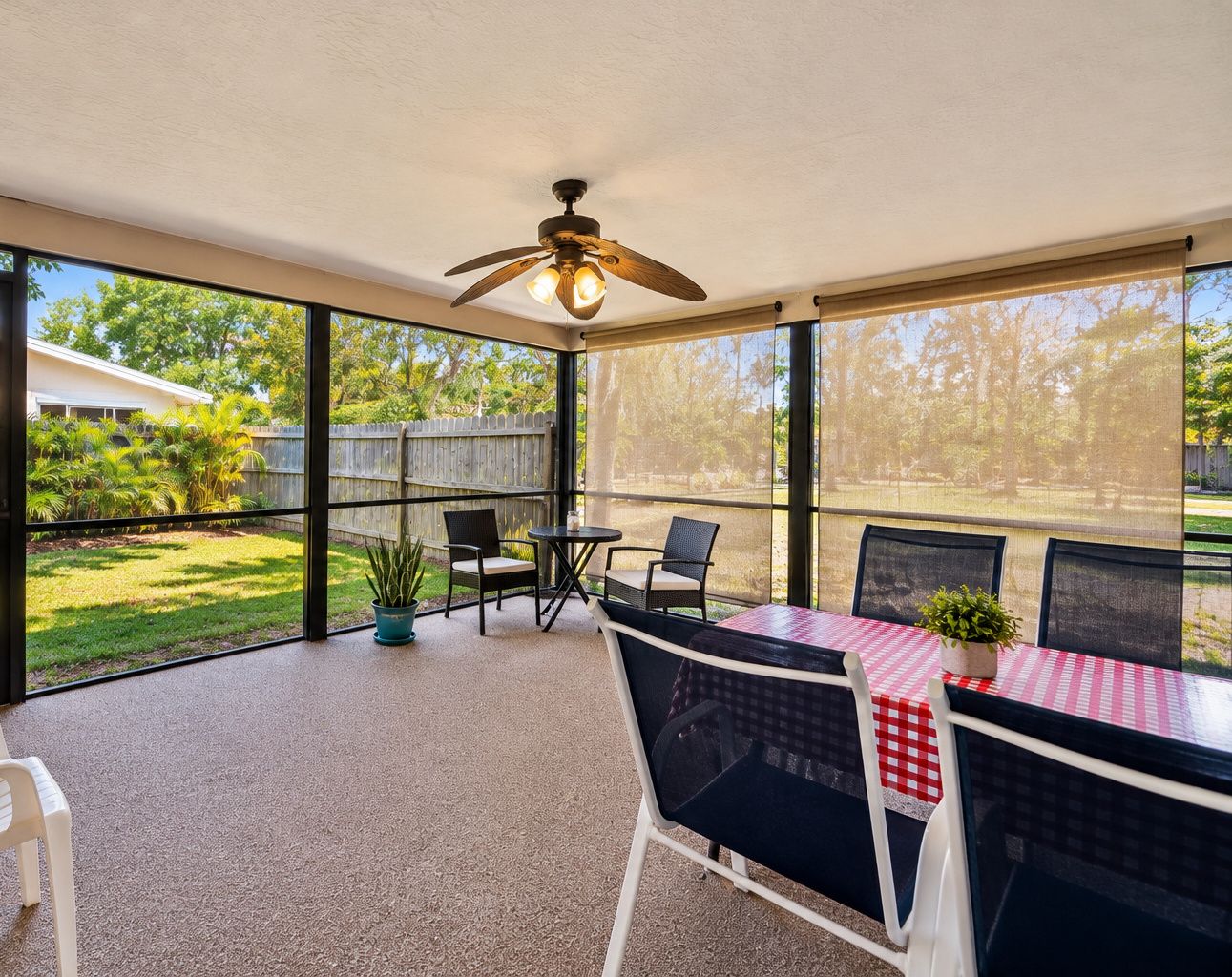 Ein überdachter Patio-Bereich mit Tisch und Stühlen, einem Deckenventilator und Blick auf einen Garten.
