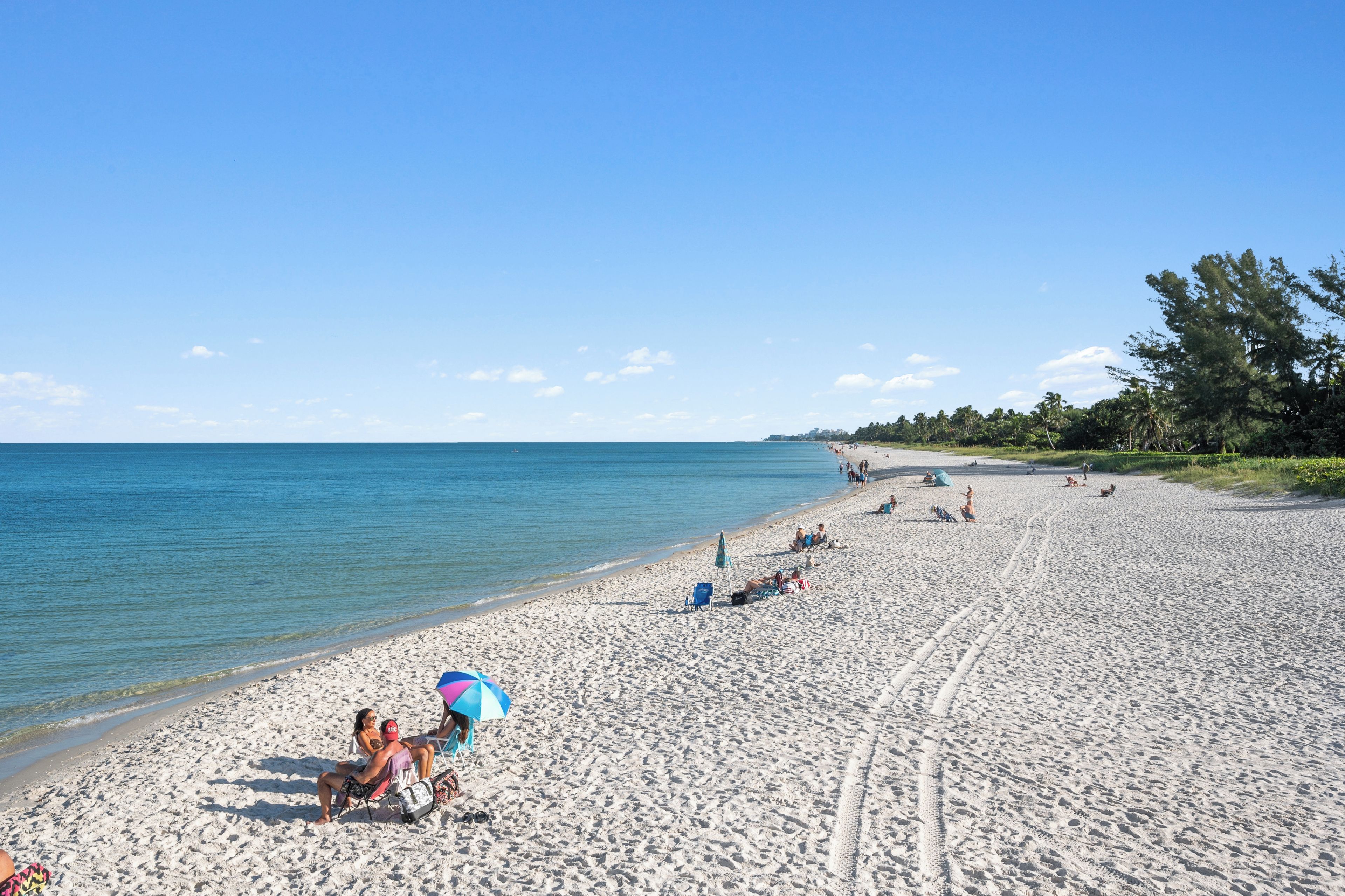 A sandy beach with clear skies, a few people, and a distant shoreline.