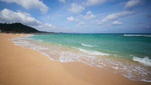 Una playa con agua turquesa cristalina, una orilla arenosa y una vista distante de un paisaje montañoso.