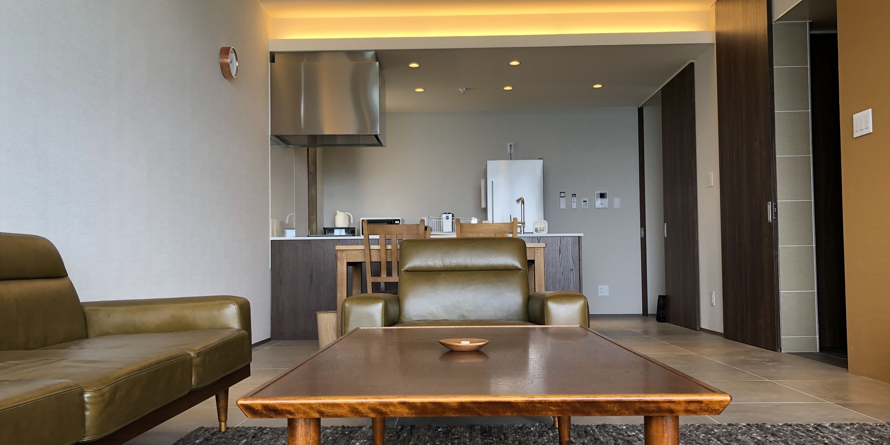 Un salon moderne avec un canapé, une table basse en bois et un coin repas comprenant des chaises, et une cuisine en arrière-plan.