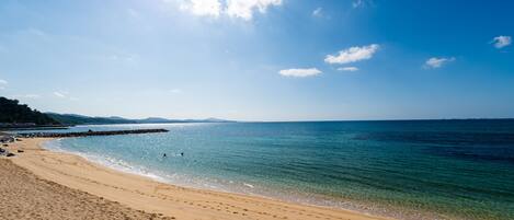 A beach with clear blue water, sandy shore, and distant mountains.