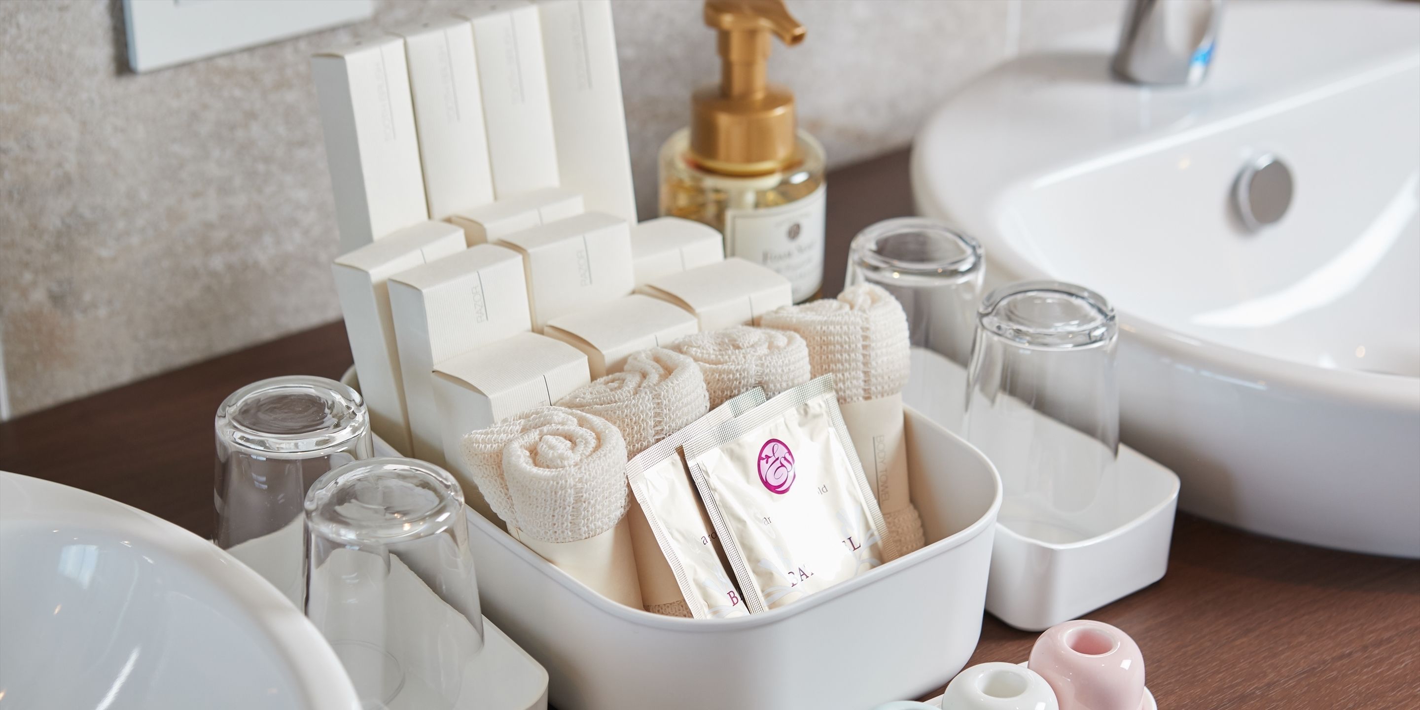 Ein Badezimmer mit einem weißen Waschbecken, einer weißen Schüssel voller Pflegeprodukte und einem weißen Handtuchhalter.