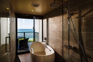 Un baño moderno con una bañera independiente, un cabezal de ducha y vista al océano.