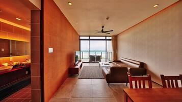 Habitación de hotel moderna con cocina, zona de estar con sofá y sillones, y un ventanal con vista al mar.