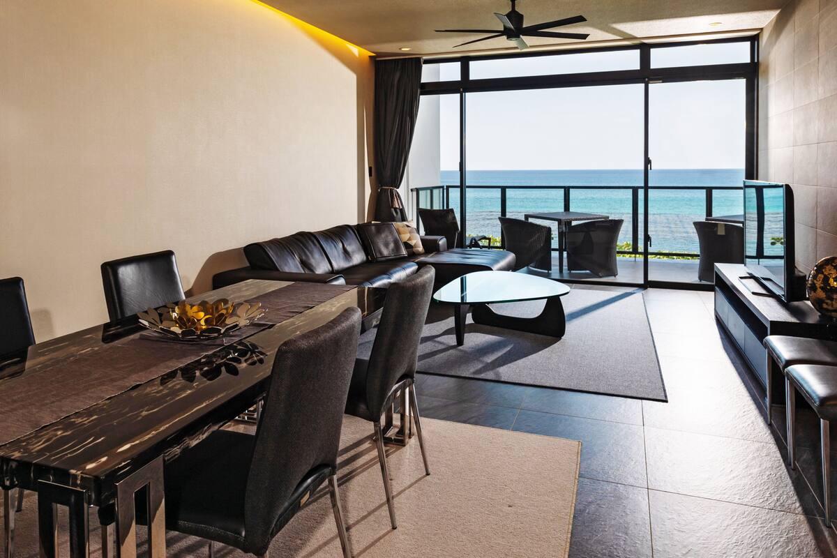 A modern living room with a dining area, large windows, and a view of the sea.