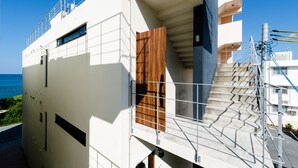 Un edificio moderno con puerta de madera, barandillas metálicas y una escalera que sube a un nivel superior.