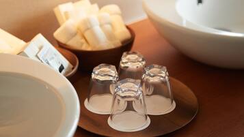 A table with a white bowl, a wooden bowl with bananas, and four clear glasses.