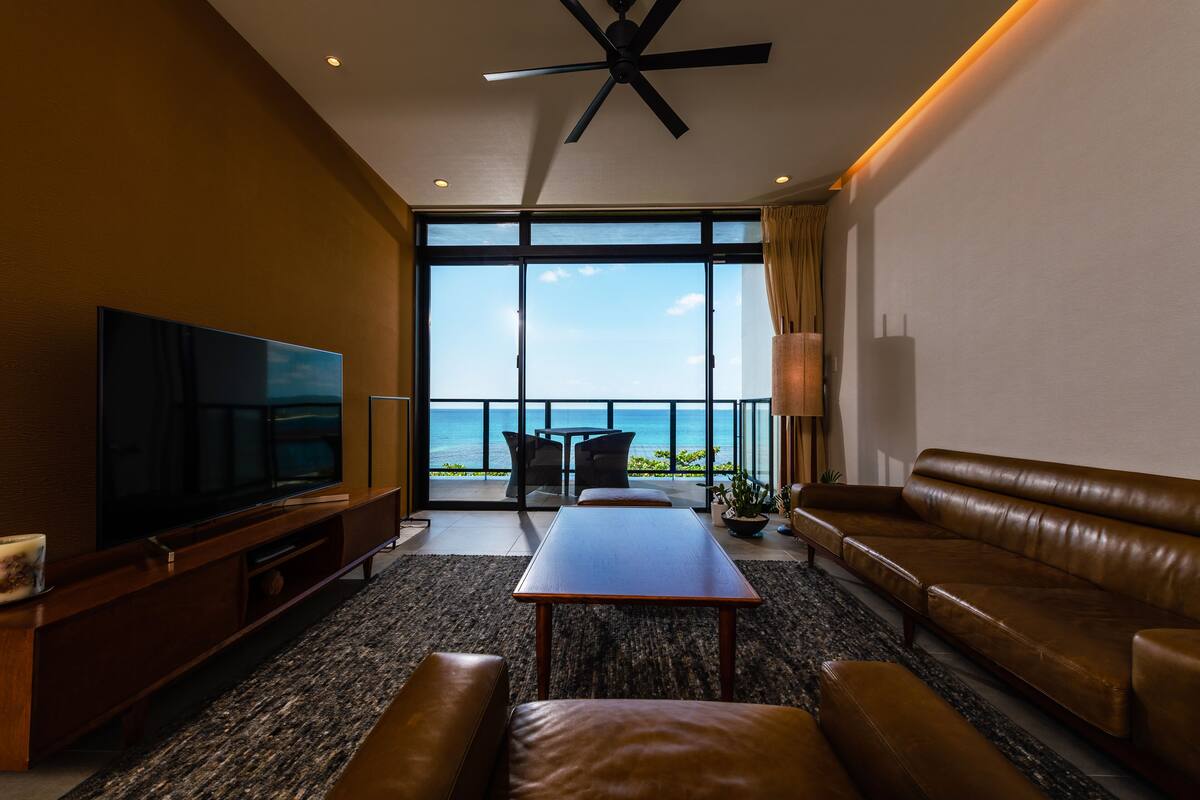 A modern living room with a large flat-screen TV, leather sofa, and a dining table.