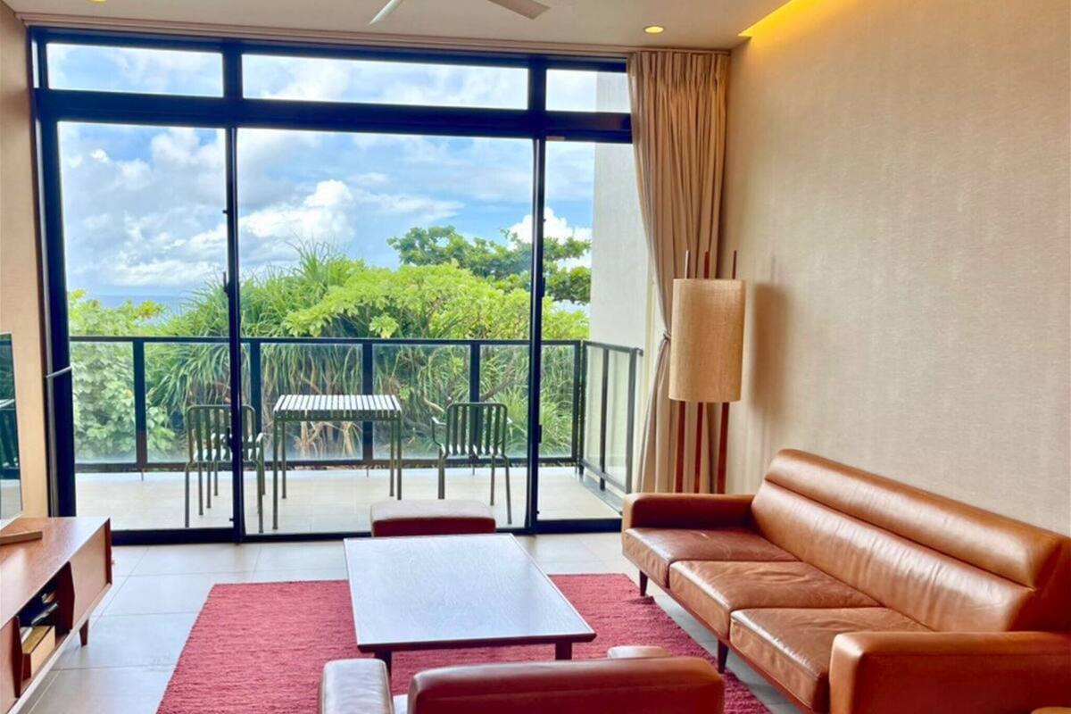A modern living room with a large sliding glass door leading to a balcony, a ceiling fan, a sofa, a coffee table, and a TV stand.