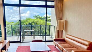 A modern living room with a large sliding glass door leading to a balcony, a ceiling fan, a sofa, a coffee table, and a TV stand.