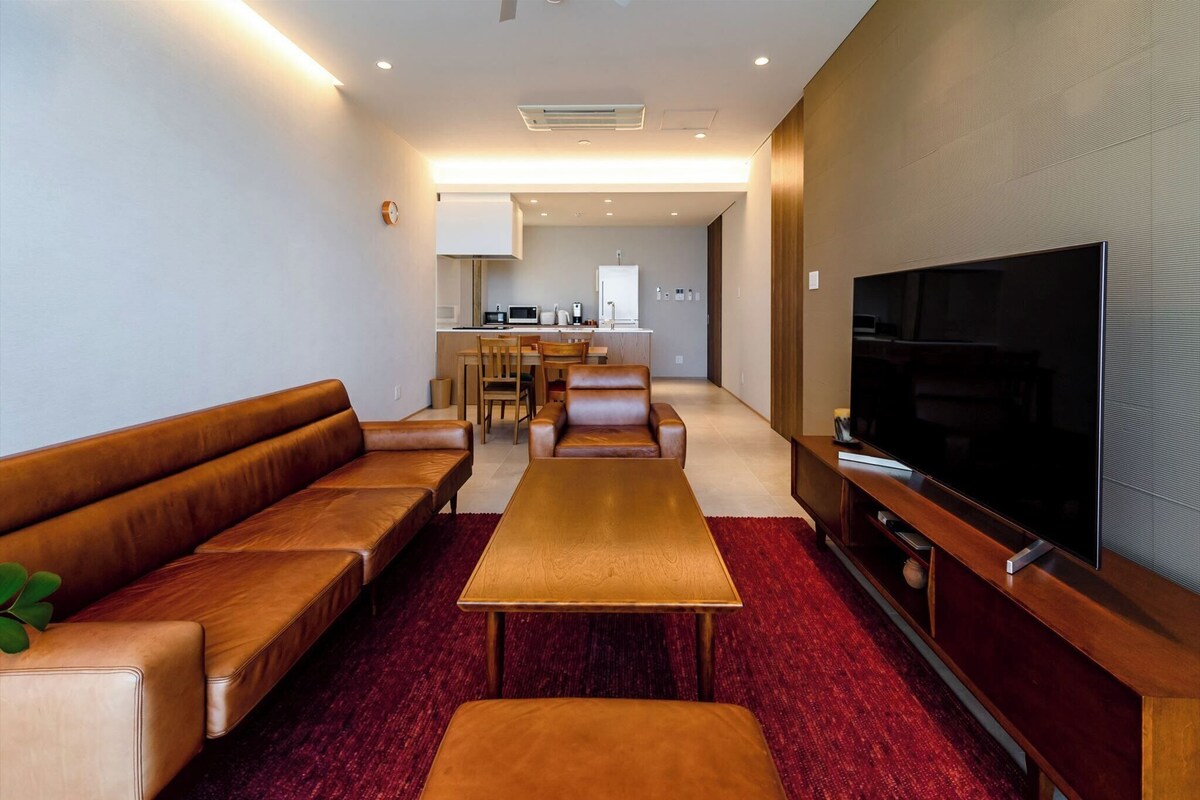 A modern living room with a sofa set, a coffee table, a TV, and a kitchen in the background.
