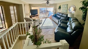 A living room with a black leather sofa, a television, and a ceiling fan.