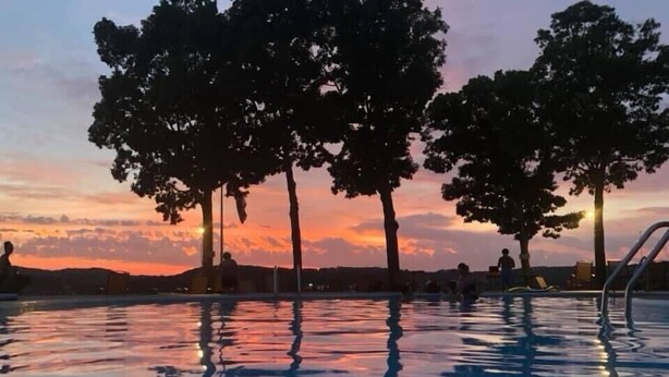 A swimming pool with trees around it during sunset.