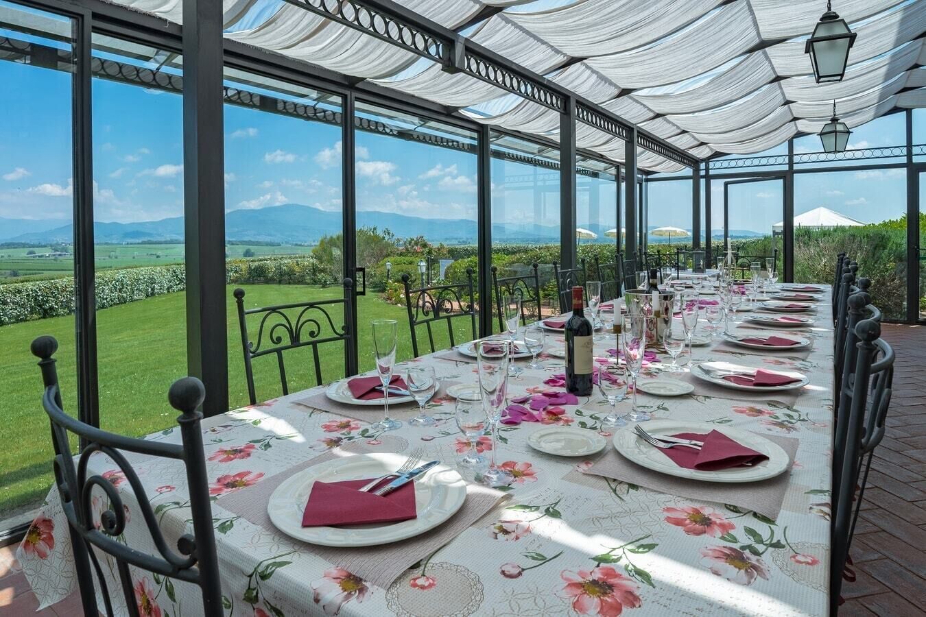 Een lange eettafel gedekt voor een maaltijd, met een prachtig uitzicht op een wijngaard en de bergen op de achtergrond.