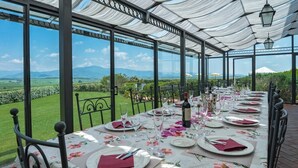 Ein langer Esstisch, gedeckt für eine Mahlzeit, mit Blick auf einen Weinberg und Berge im Hintergrund.