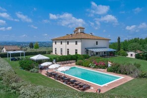 Une grande maison avec une piscine, un patio couvert et une vue sur la campagne.