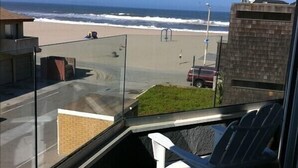 A balcony with a view of the beach and ocean. There are two white Adirondack chairs and a small grassy area. - Ocean and Beach View Townhouse at Mandalay Beach in Oxnard, California (Oxnard)