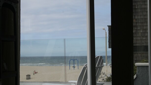 A view from inside a room with a glass door overlooking a beach. There are two white chairs and a small table with a hot tub visible. - Ocean and Beach View Townhouse at Mandalay Beach in Oxnard, California (Oxnard)