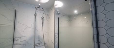 A modern bathroom with a glass shower enclosure, marble walls, and a ceiling light fixture.