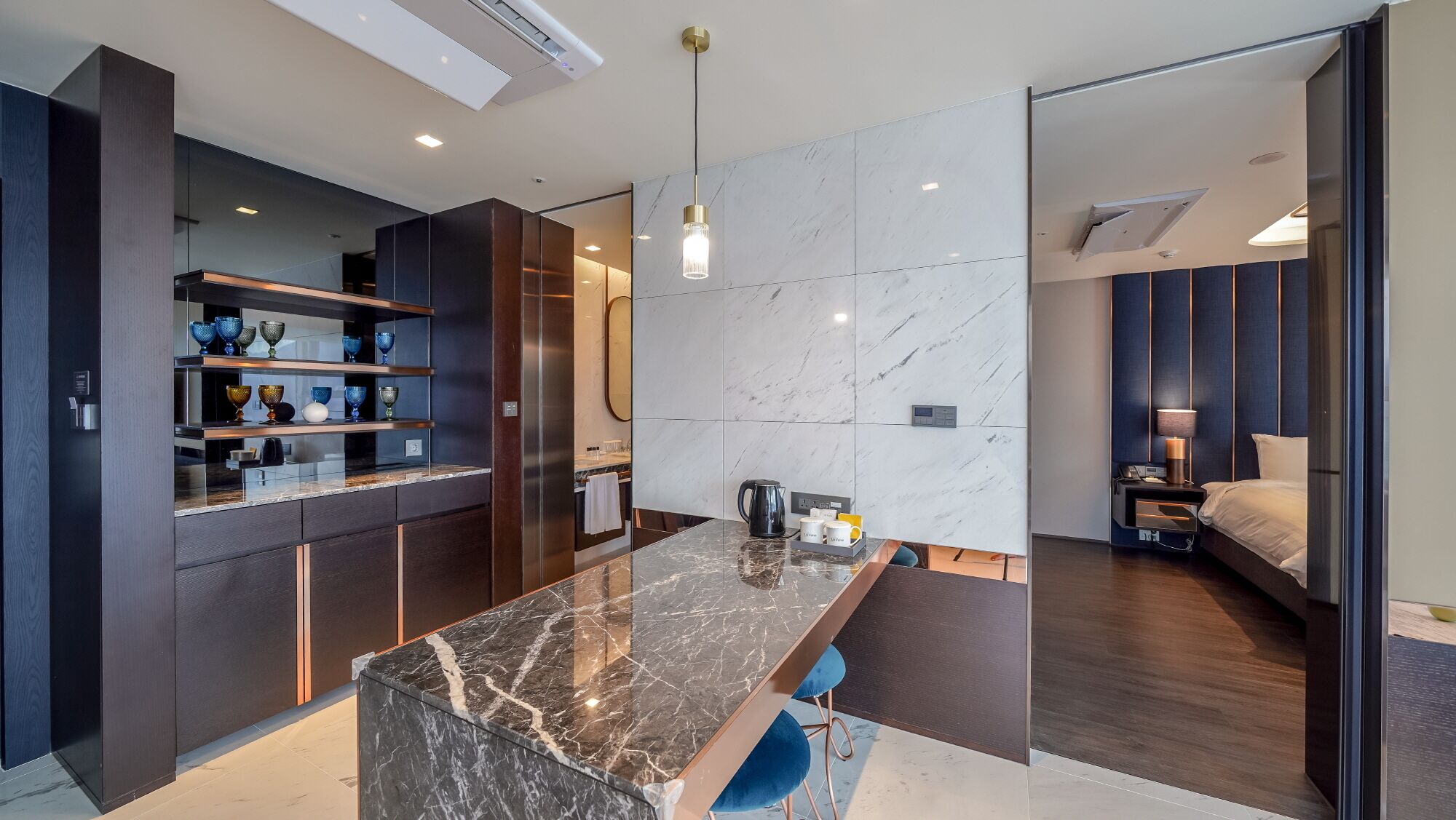 A modern kitchen with dark cabinetry, a marble island, and a pendant light.