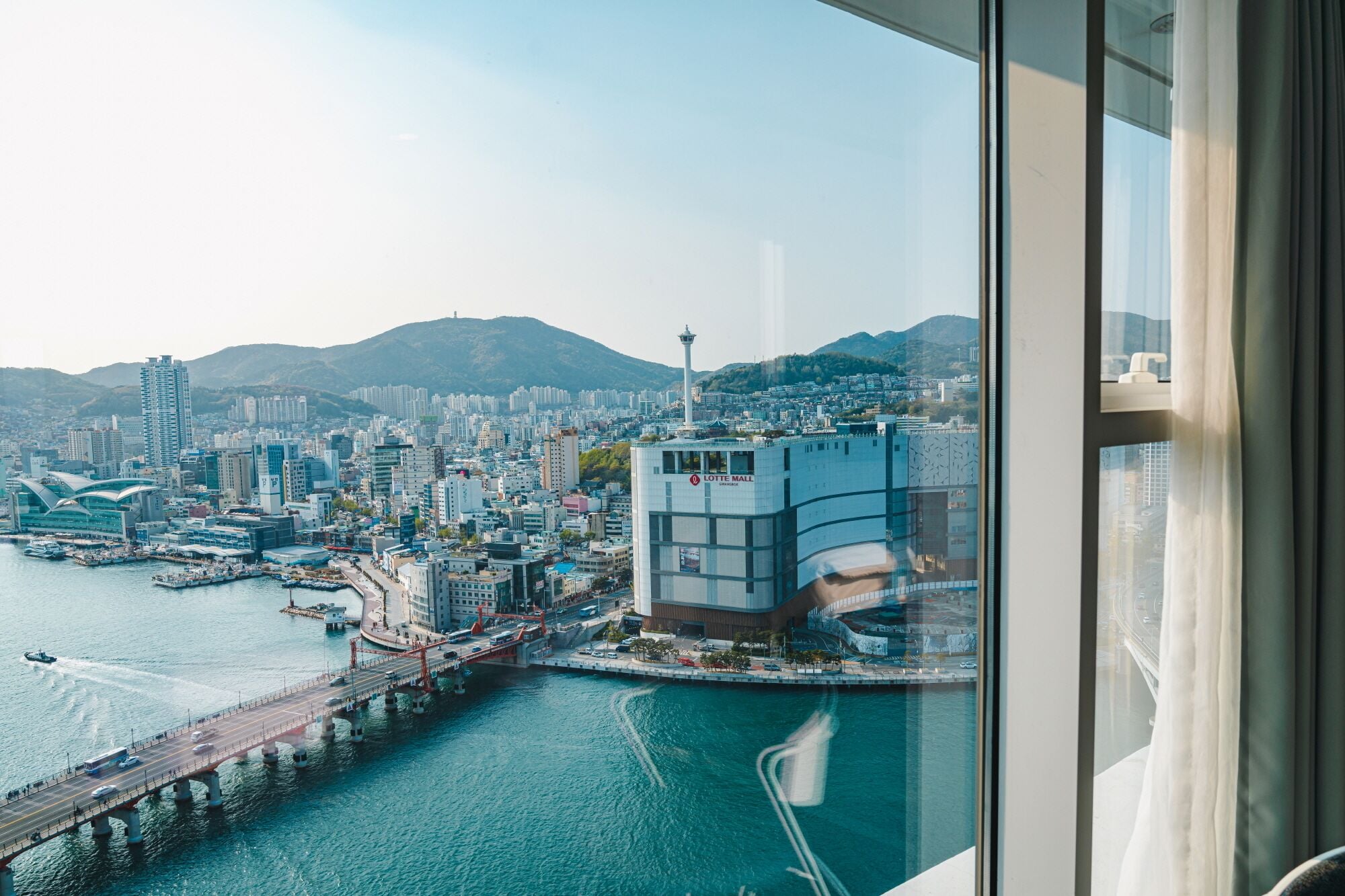A cityscape with a prominent Lotte Mall building, a bridge, and a body of water.