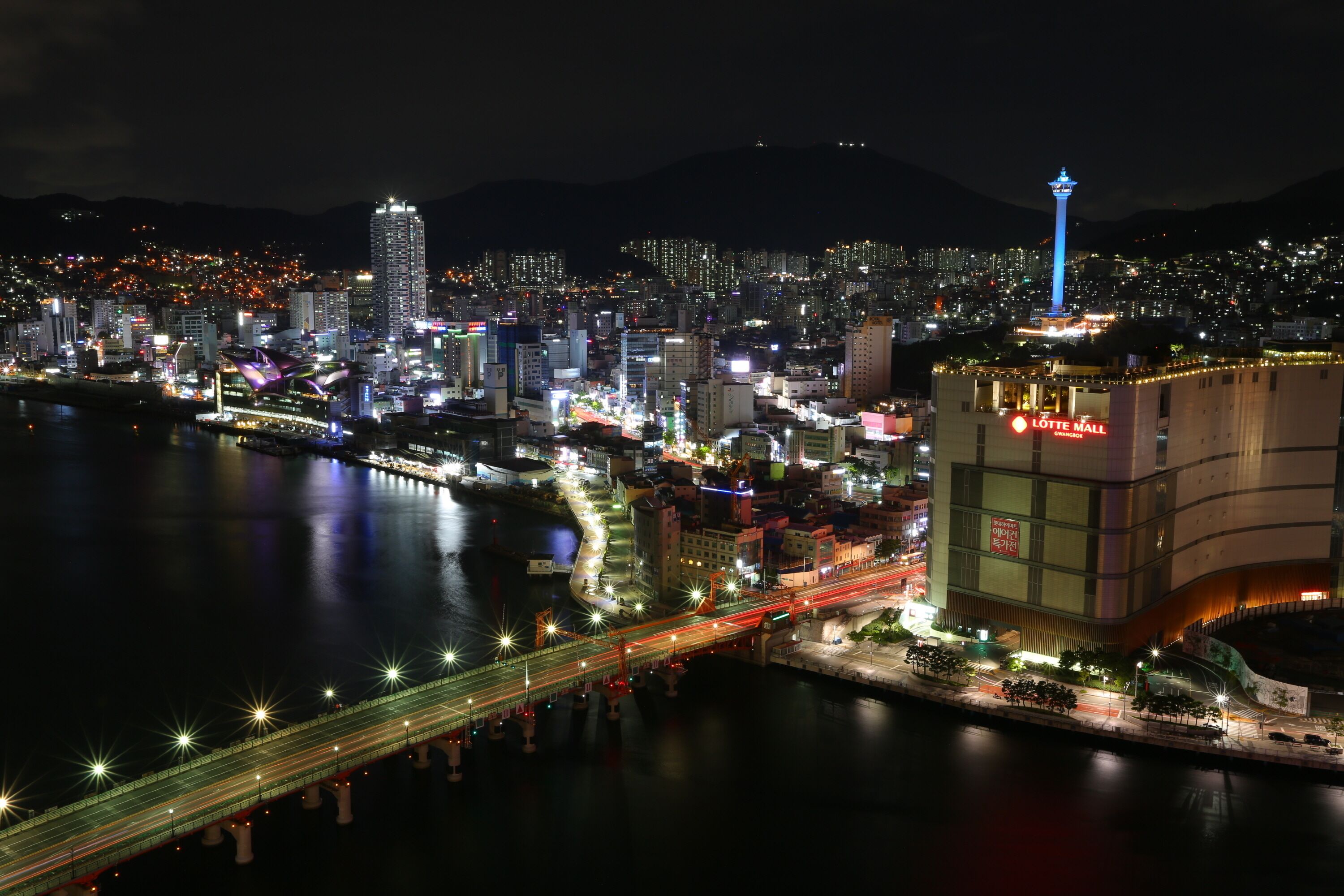 A nighttime cityscape with a prominent building featuring a sign for Lotte Mall.