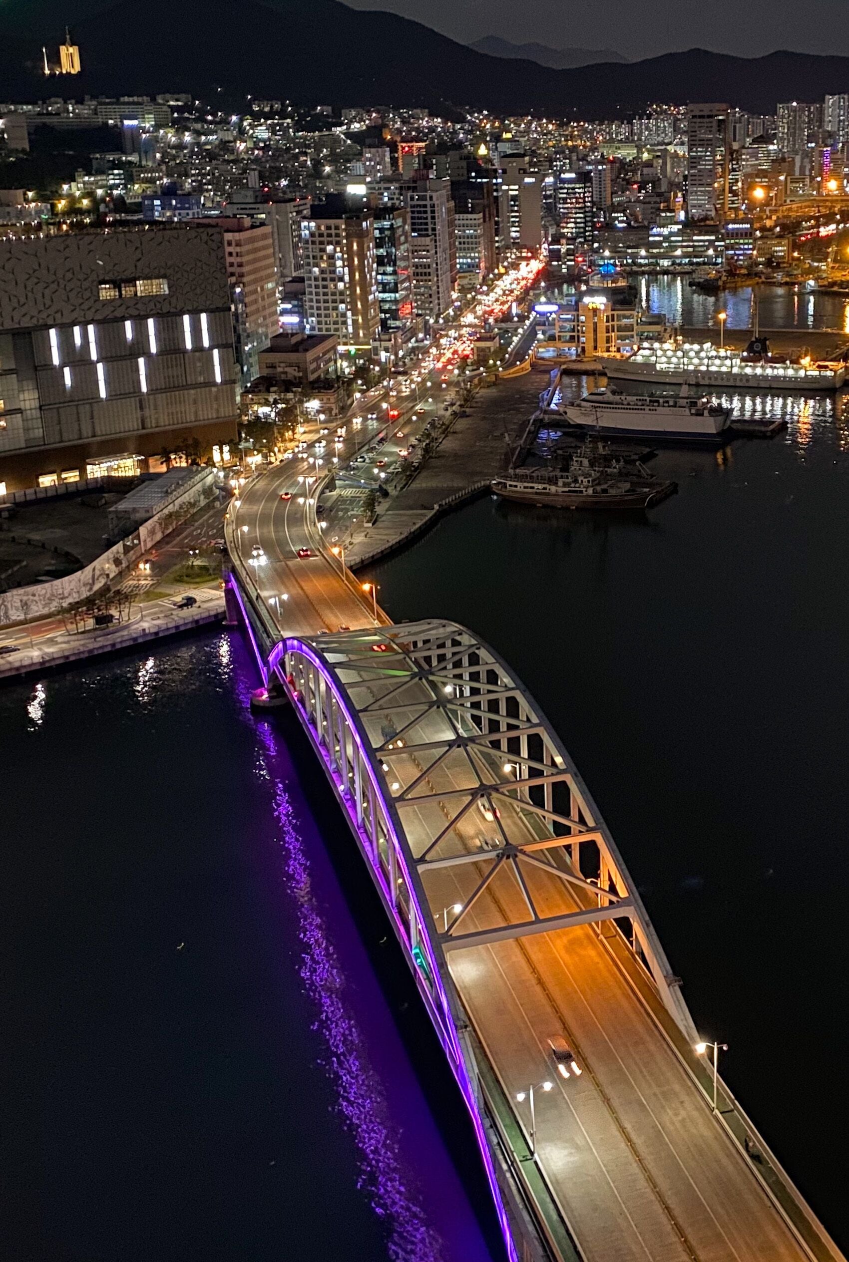 Un paisaje urbano nocturno con un puente sobre un río, con calles y edificios iluminados.
