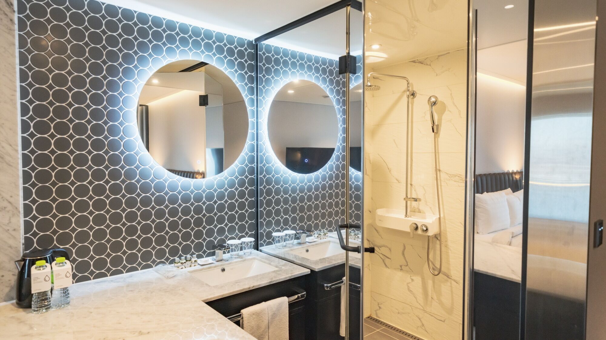 A modern bathroom with two sinks, a shower, and a large mirror.