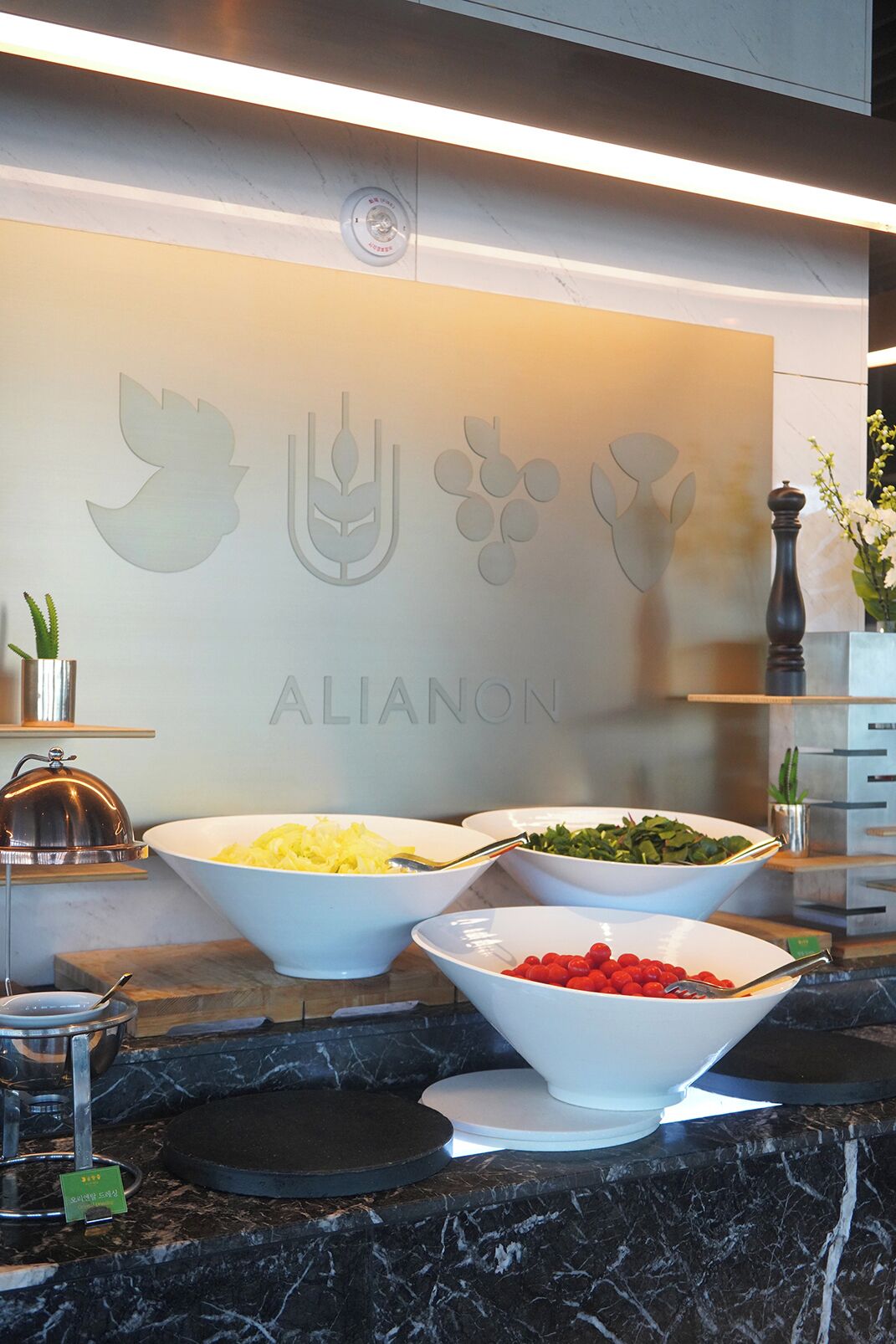 A buffet area with various food items in bowls, a wall with a logo, and a marble countertop.