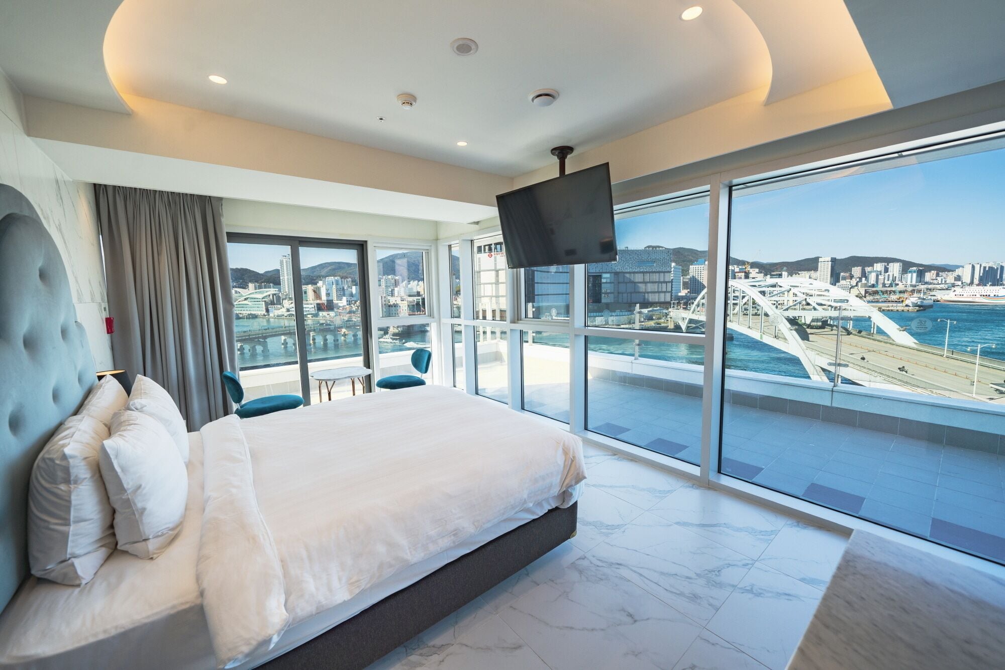 Un dormitorio de hotel moderno con una cama grande, un televisor y vistas a la ciudad.
