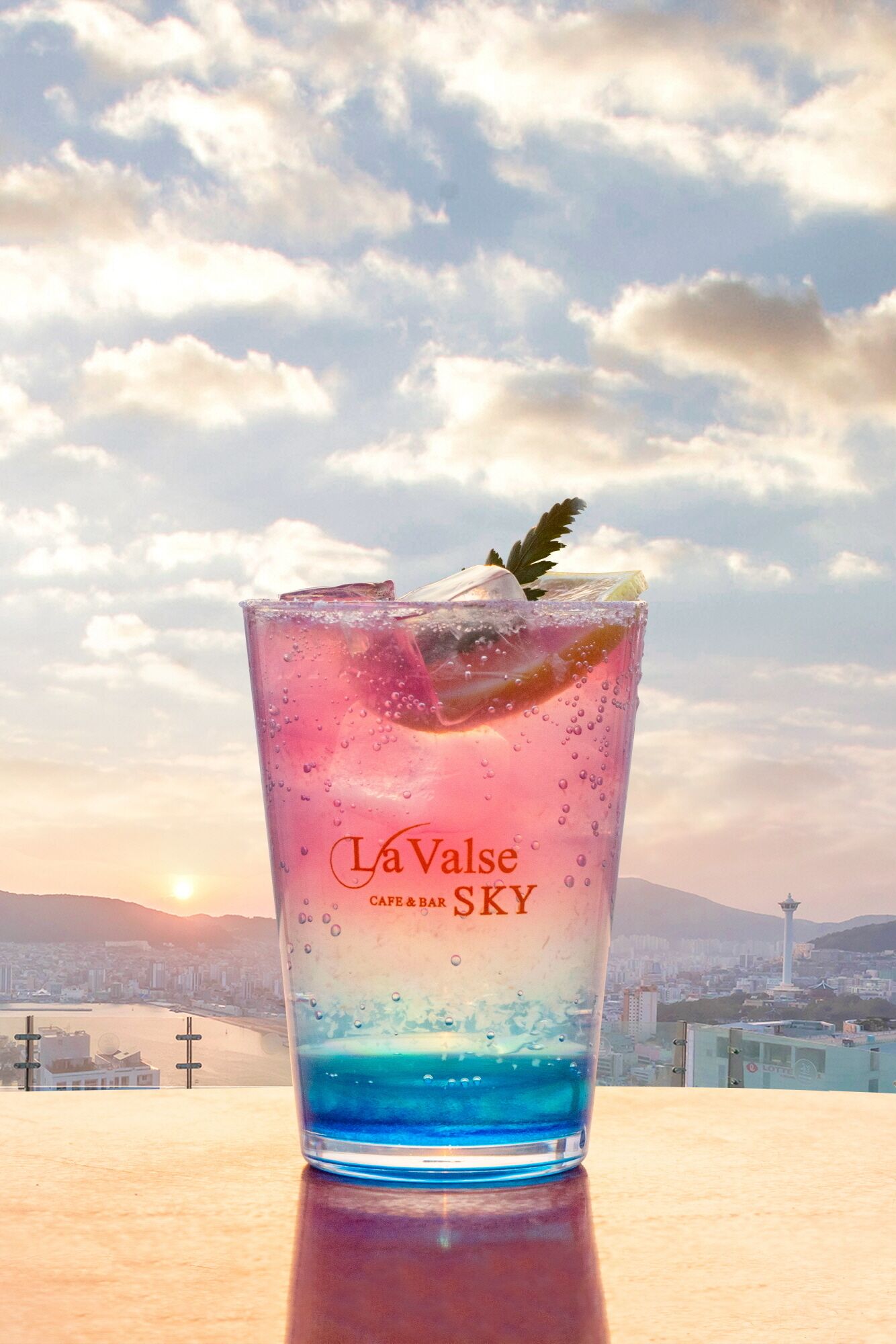 Un vaso de bebida con un paisaje urbano y montañas al fondo.